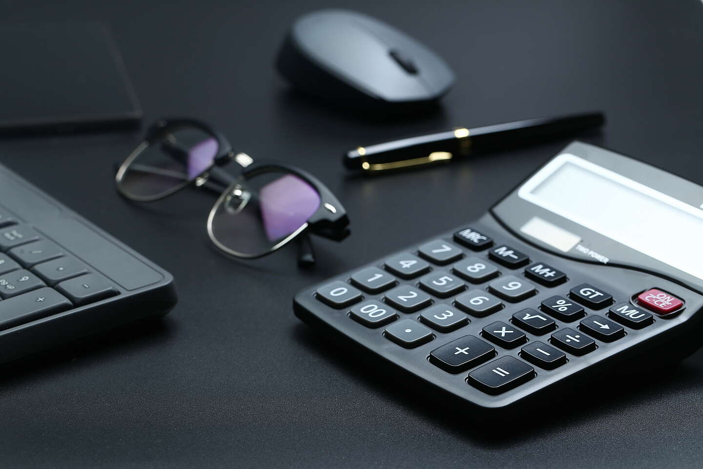Ein Pult mit einem Taschenrechner, eine Brille, Maus und Tastatur